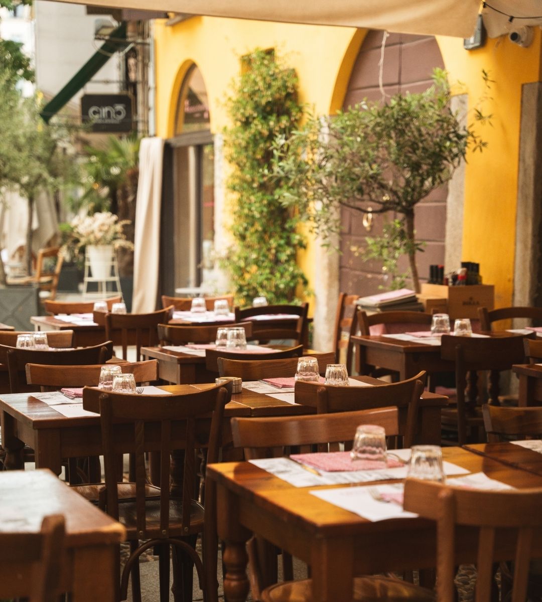 Tavoli all'aperto e sedie in legno nel dehors di un ristorante storico milano