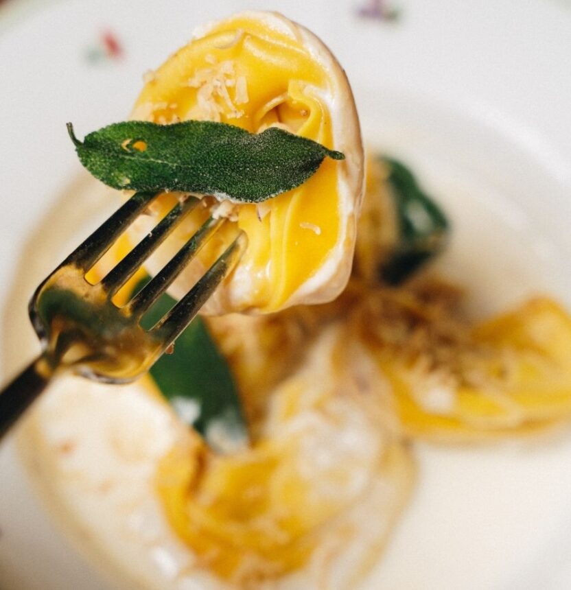 Primo piano di un tortello alla zucca con foglia di salvia e granella di castagne di Rosso Brera Primo piano di un tortello alla zucca con foglia di salvia e granella di castagne di Rosso Brera